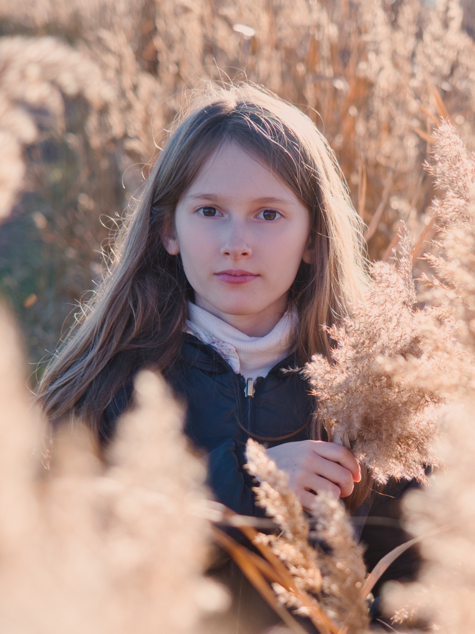 Une fille au regard sérieux tient une plante dans un champ doré.