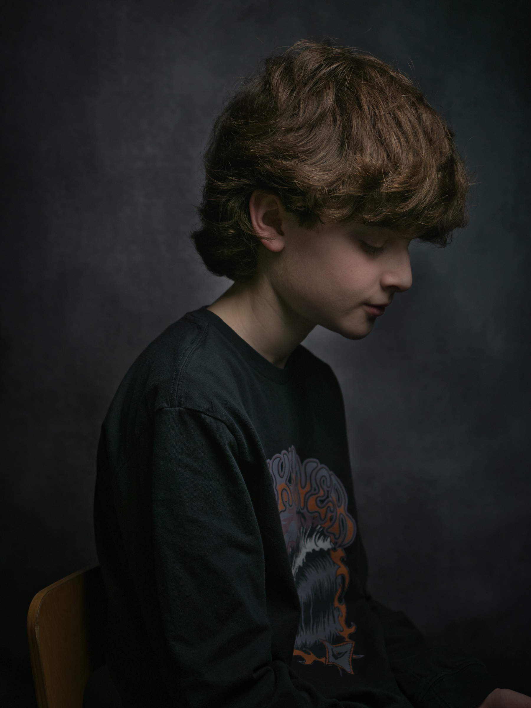 Un garçon assis, silhouette de profil, cheveux bouclés, regard pensif.