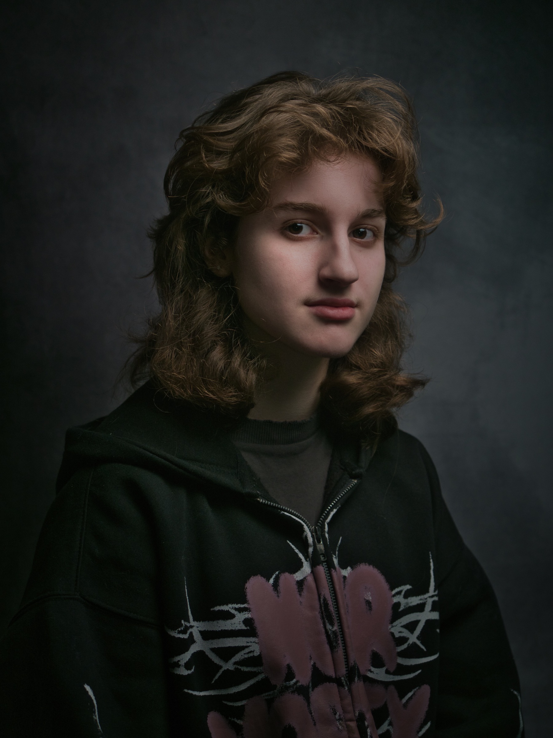 Portrait d'une jeune femme avec cheveux mi-longs et sweat à capuche noir, regard sérieux.