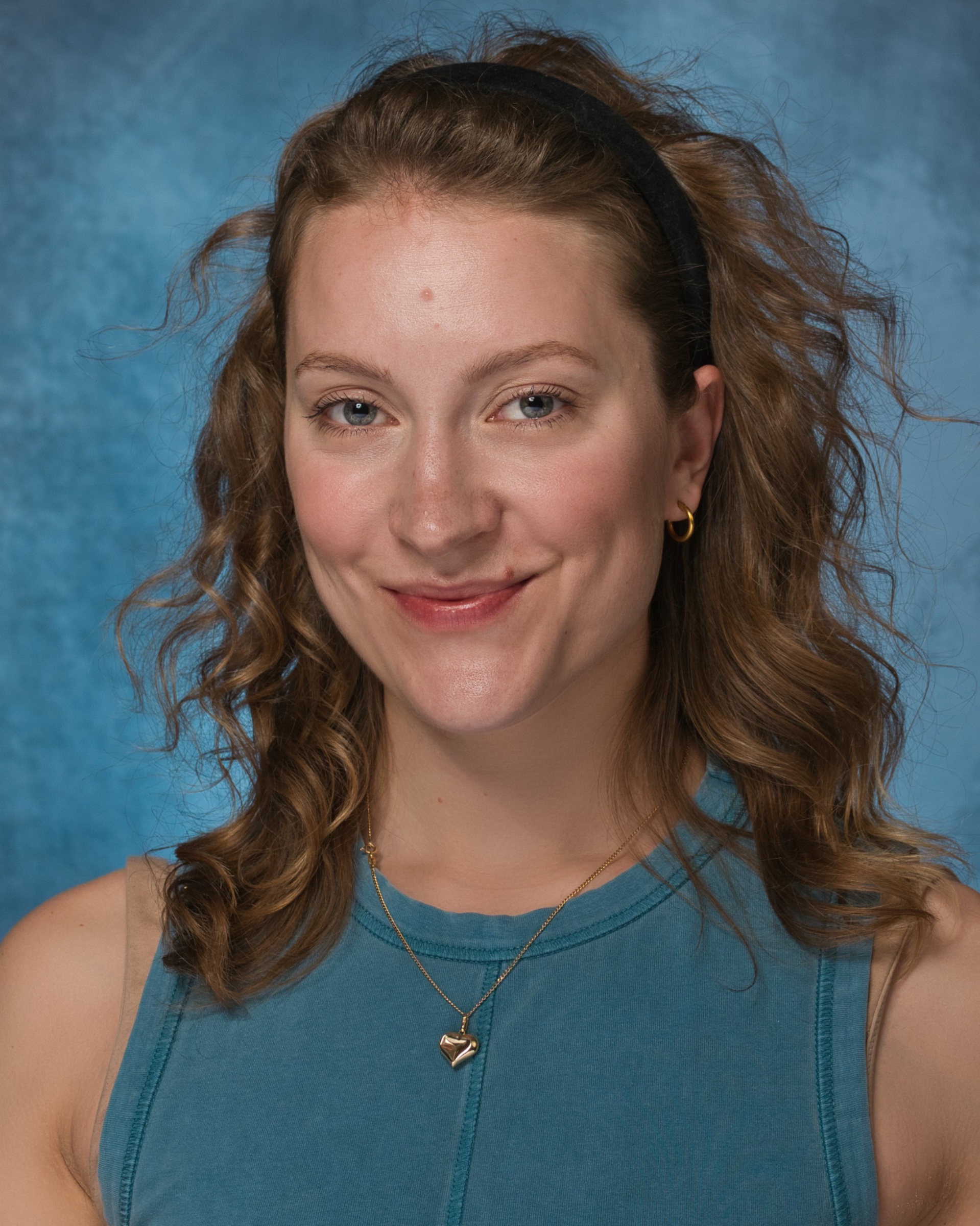 Femme souriante avec des cheveux bouclés, portant un haut bleu et un collier.