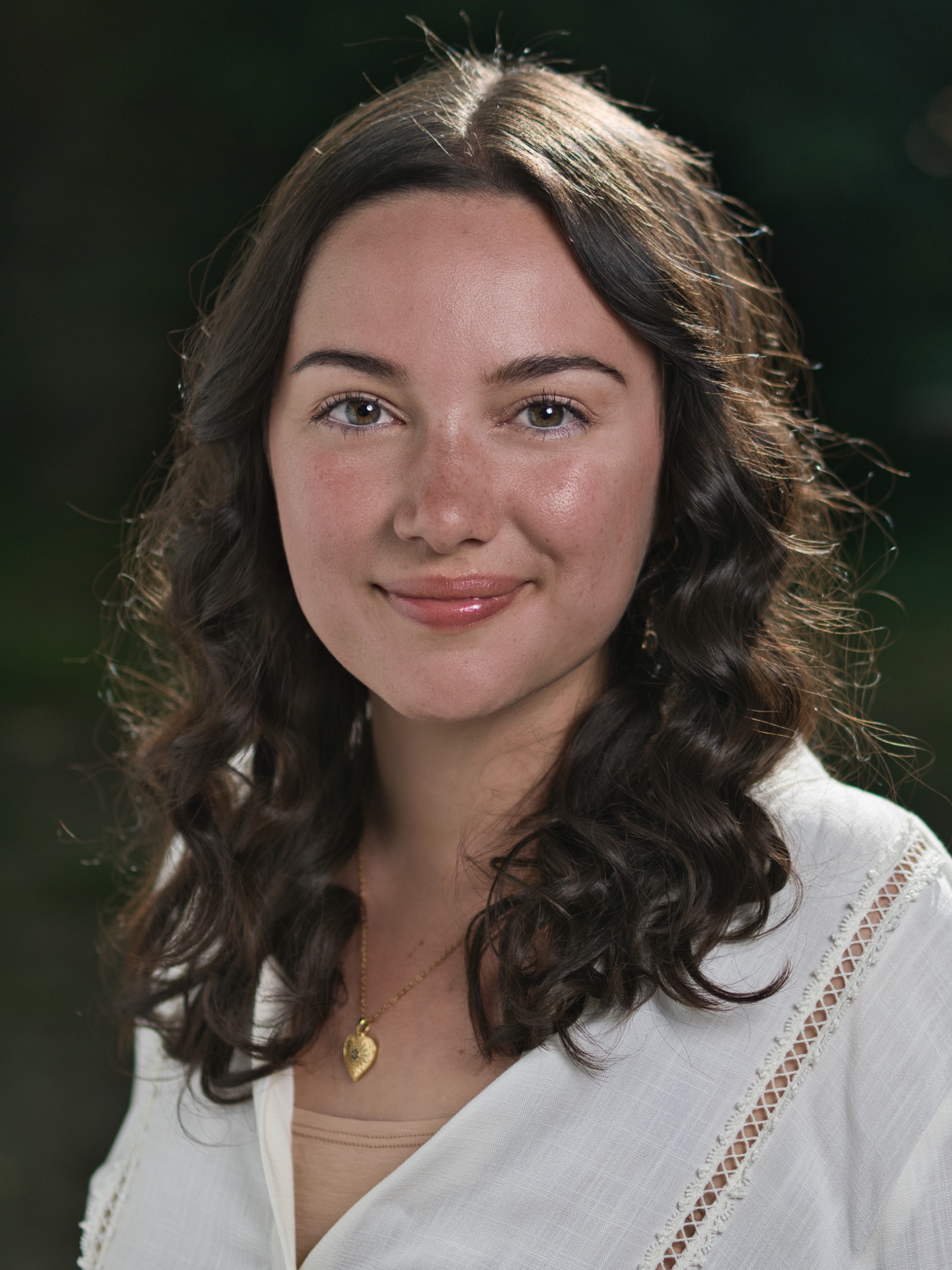 Portrait d'une jeune femme aux cheveux bouclés, souriante, vêtue d'une blouse claire.