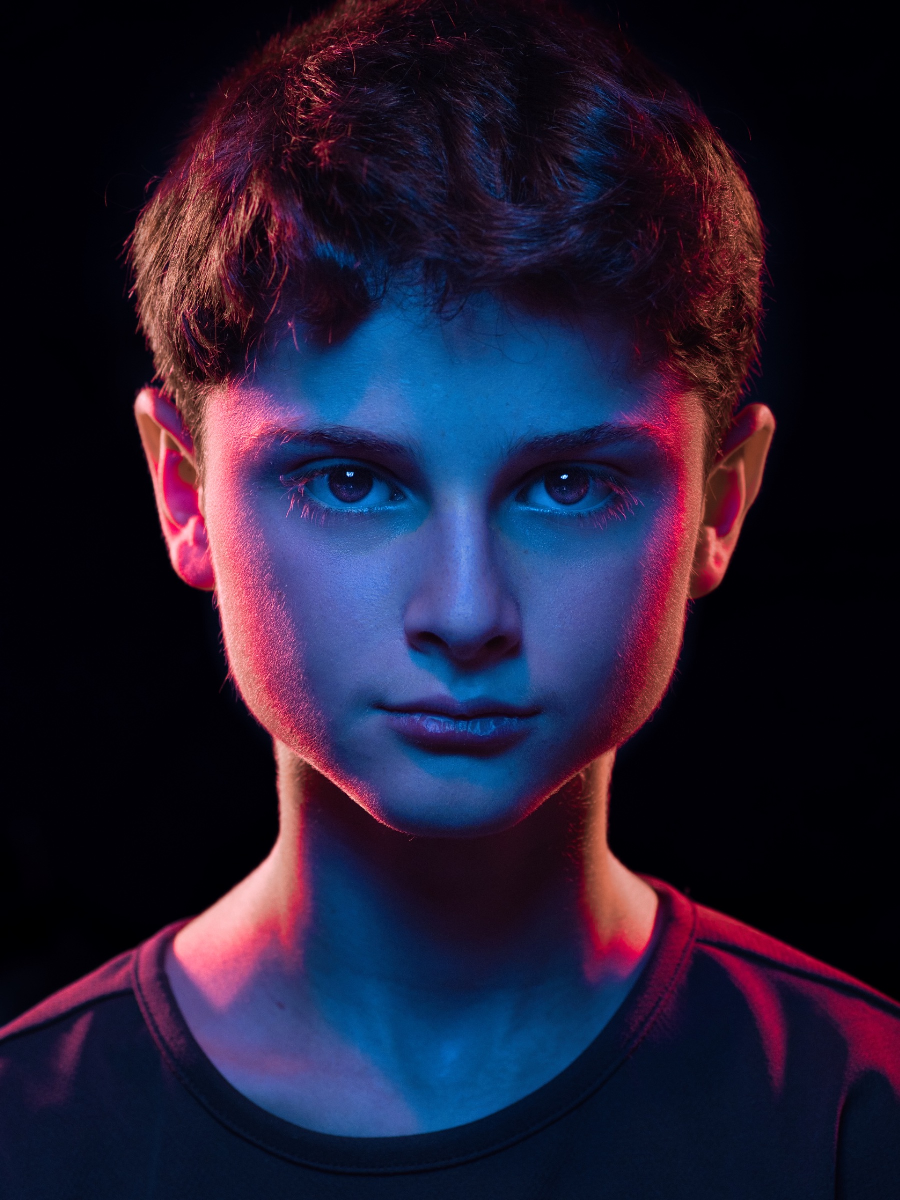 Un jeune garçon avec un regard intense, éclairé par des lumières bleues et roses.