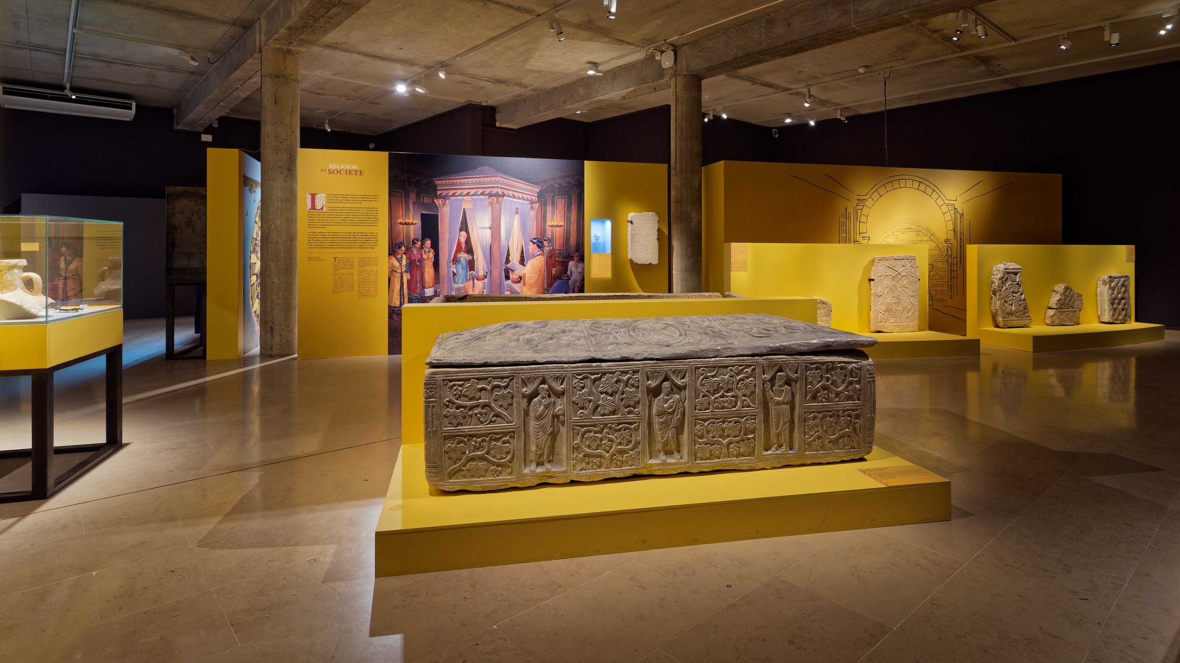 Une salle d'exposition avec une tombe en pierre et des panneaux colorés.