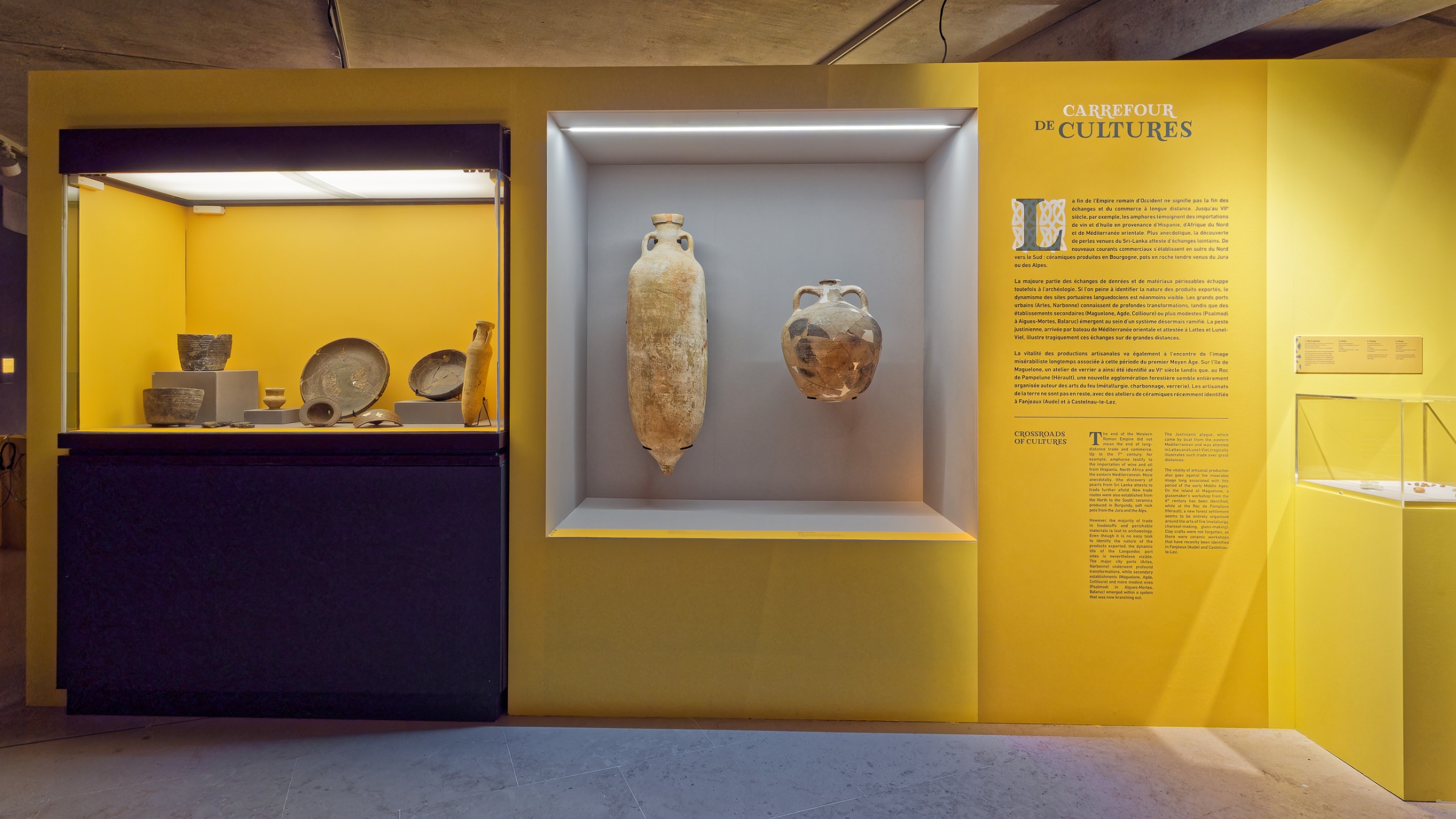 Exposition avec pots en argile et amphore sur fond jaune. Informations à côté.