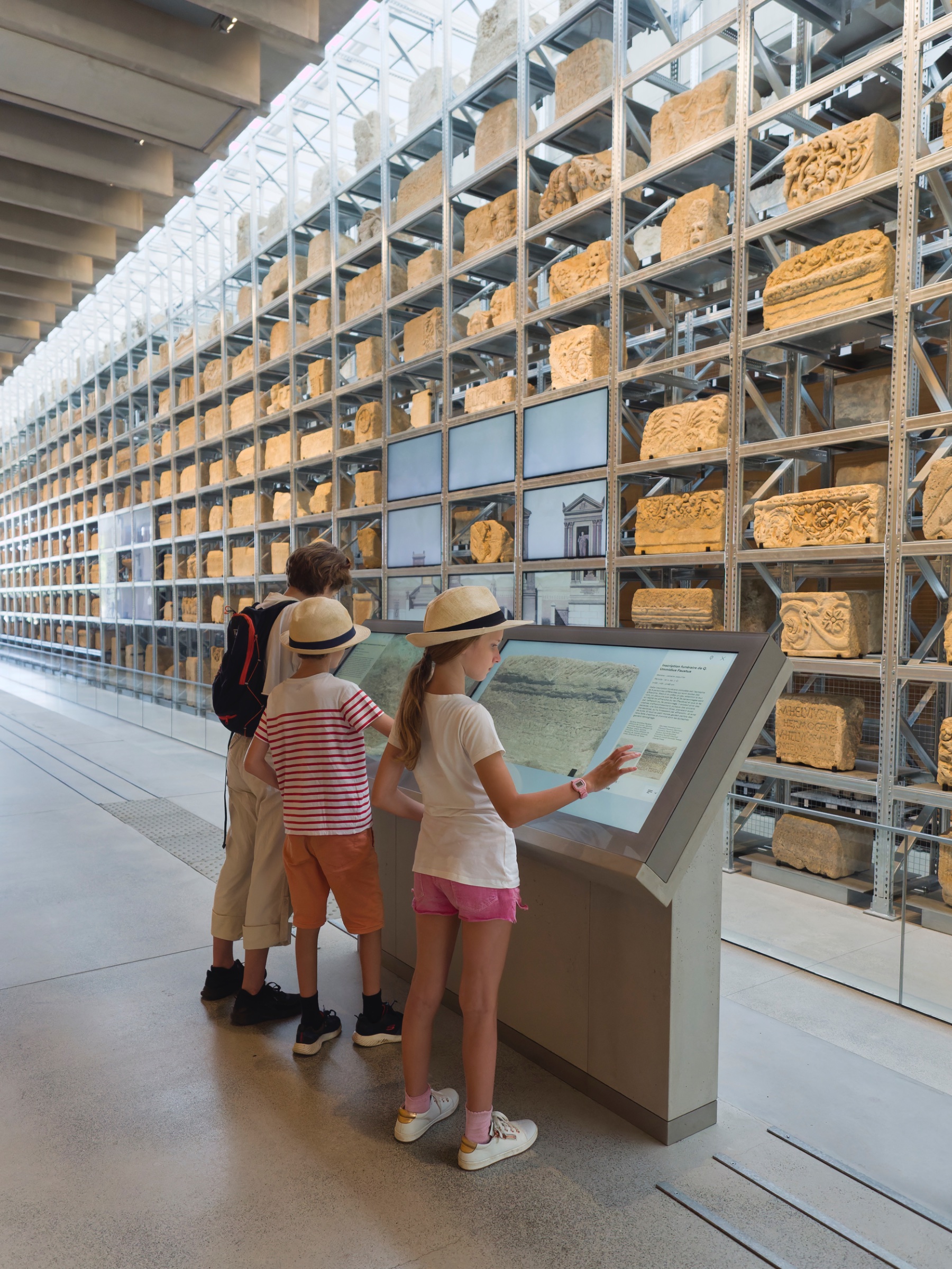 Trois enfants observent des sculptures anciennes dans un musée moderne.