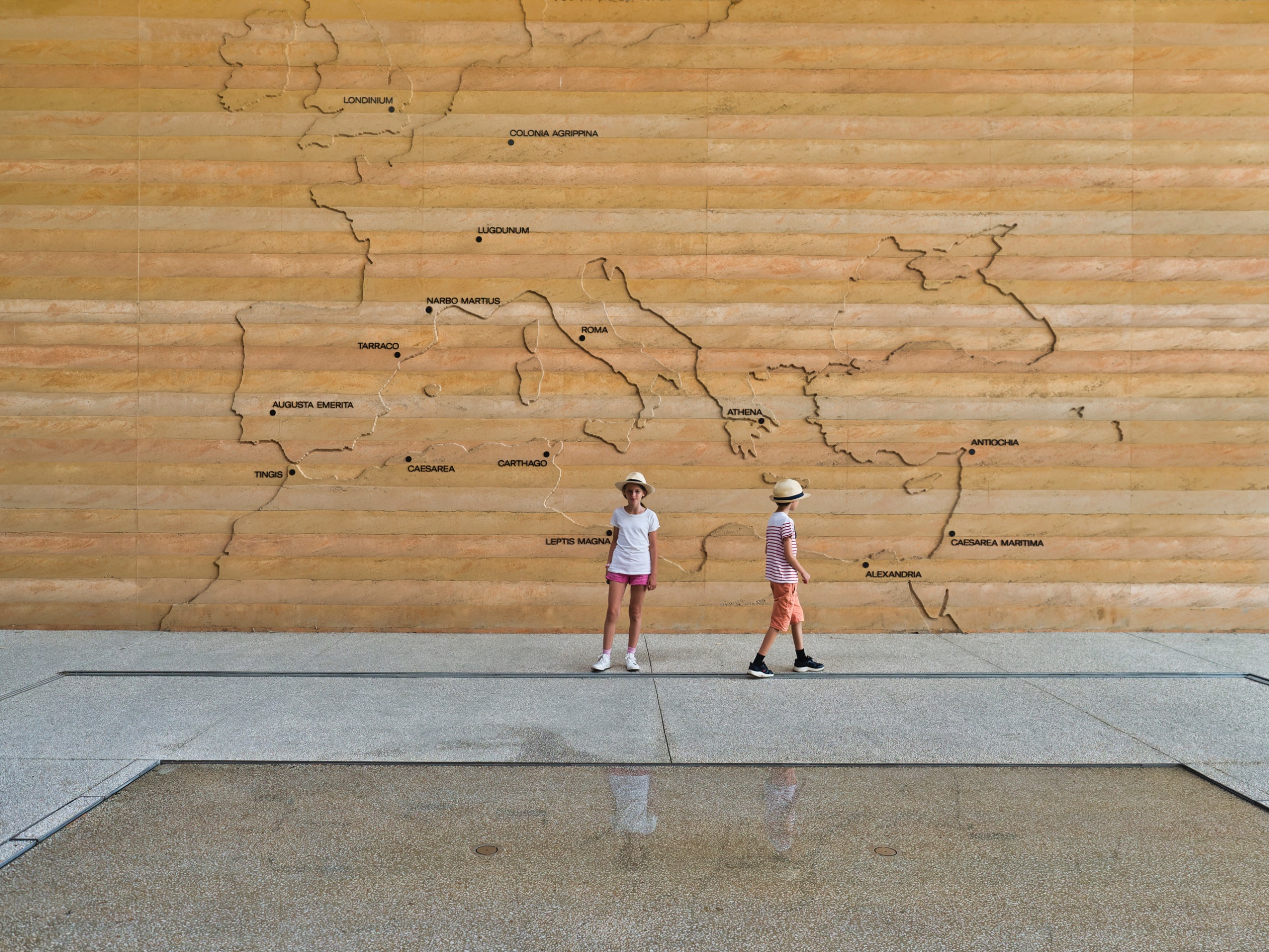 Deux enfants marchent devant un mur gravé, représentant une carte de l'Europe.