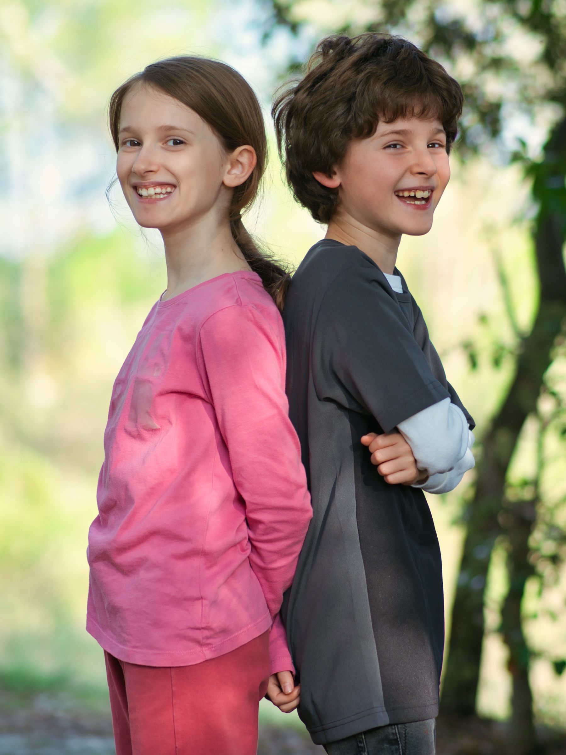 Deux enfants se tenant dos à dos, souriant, en plein air.