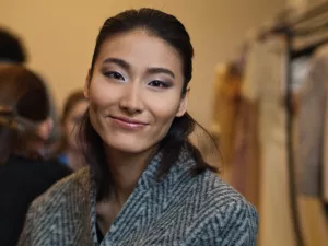 Femme souriante avec un maquillage subtil, portant un pull en laine gris.