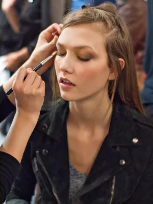 Femme avec un maquillage artistique, les yeux fermés, recevant des retouches.
