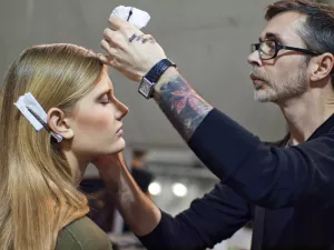 Un maquilleur applique du maquillage sur une mannequin dans les coulisses d'un défilé.