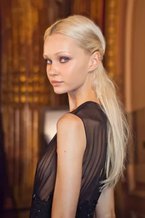 Femme au teint clair, cheveux longs et blonds, regard sérieux, vêtue d'une robe noire élégante.