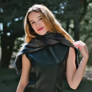 Femme avec un foulard, vêtue d'une robe noire, en arrière-plan naturel.
