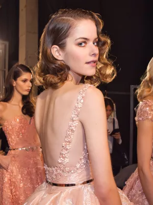 Femme en robe de soirée rose ornée, regardant en arrière, cheveux bouclés.