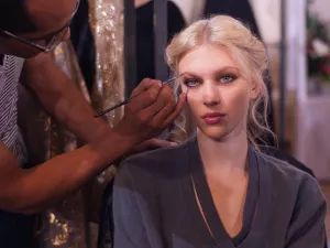 Un artiste maquilleur applique du maquillage sur une modèle aux cheveux blonds.