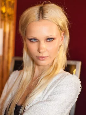 Femme aux cheveux blonds et longs, yeux clairs, regard intense, fond flou.