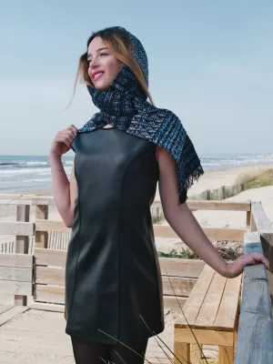 Femme souriante sur une plage, vêtue d'une robe en cuir et d'un châle bleu.