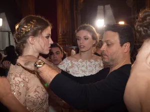 Une maquilleuse ajuste une robe à une mannequin dans une ambiance de backstage.