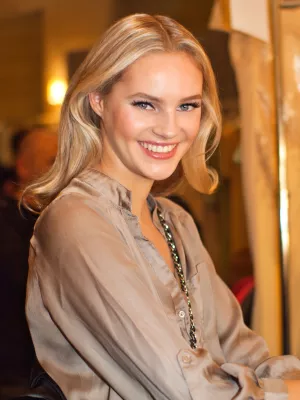 Femme souriante aux cheveux blonds, vêtue d'une blouse satinée, ambiance chaleureuse.