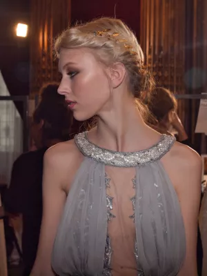 Femme en robe légère, élégante, avec un chignon et un maquillage sophistiqué.