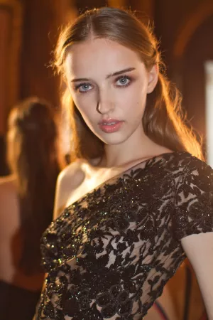 Femme élégante avec une robe noire ornée, cheveux lâchés, regard captivant.