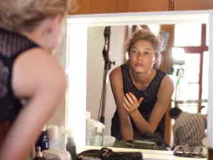Femme se préparant devant un miroir, avec des produits de beauté autour d'elle.