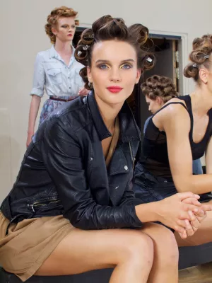 Femme avec des rouleaux dans les cheveux, vêtue d'une veste en cuir, assise devant un miroir.