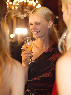 Femme souriante en robe colorée, tenant un verre, dans une ambiance élégante.