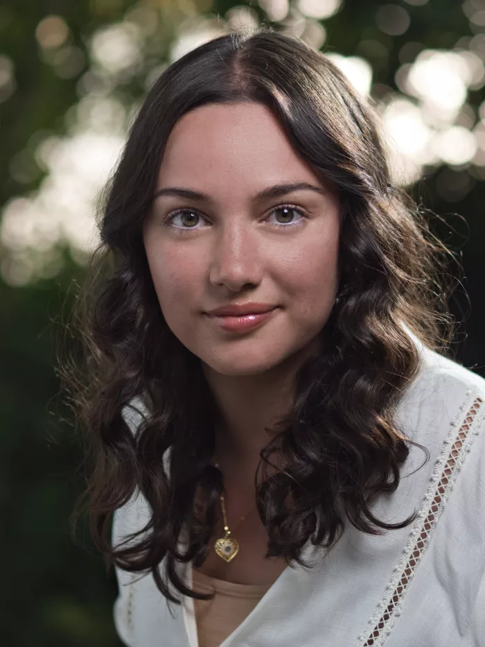 Jeune femme souriante avec des cheveux bouclés, en arrière-plan flou et verdoyant.