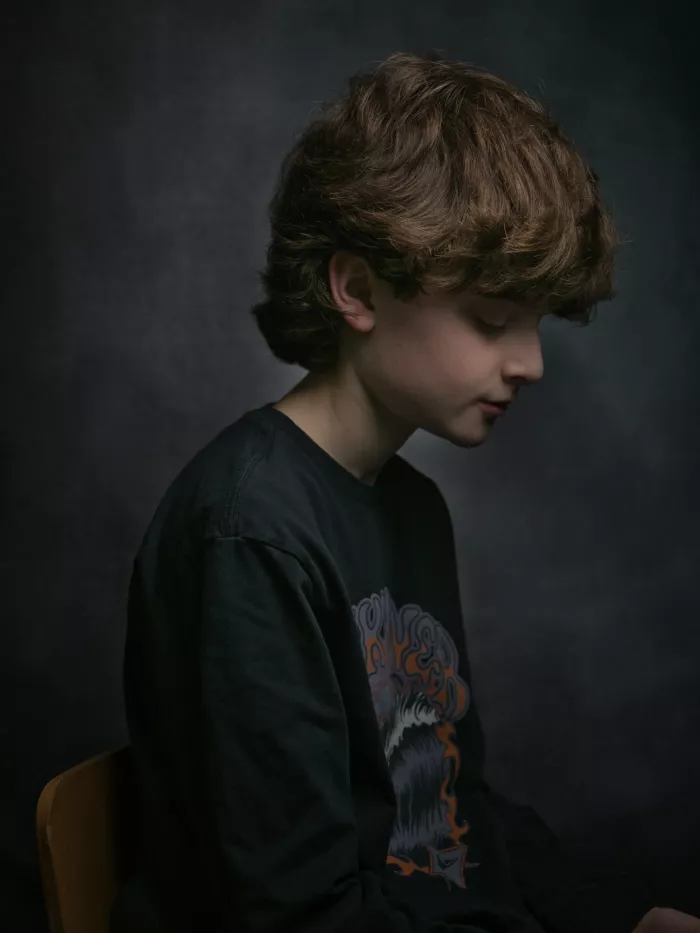 Un garçon assis, silhouette de profil, cheveux bouclés, regard pensif.
