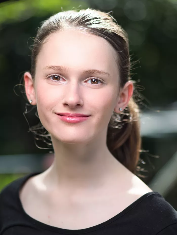 Portrait d'une jeune femme souriante, avec des cheveux longs et un fond flou.