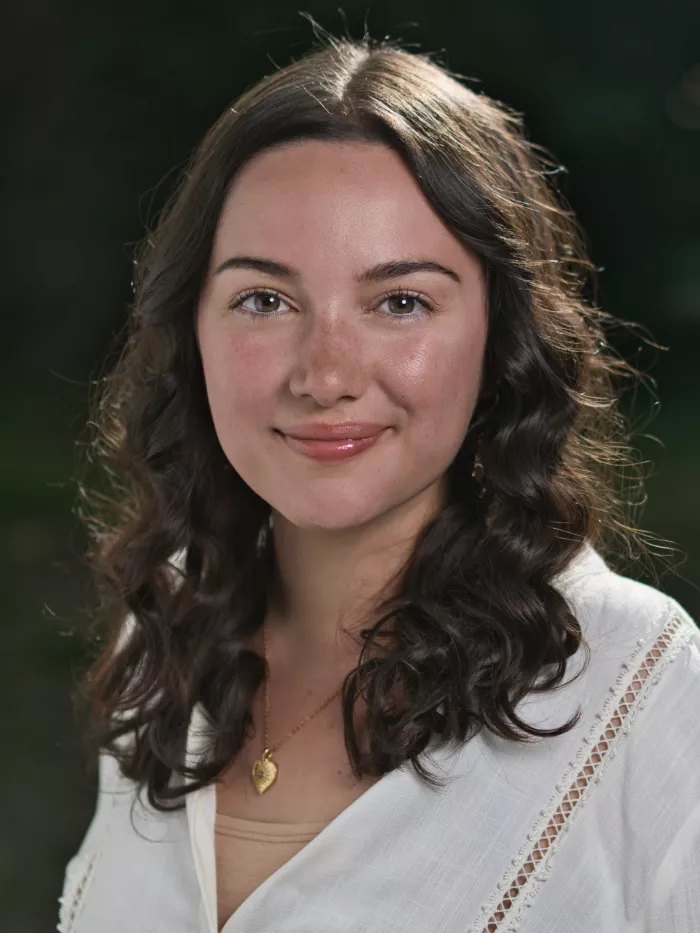 Portrait d'une jeune femme aux cheveux bouclés, souriante, vêtue d'une blouse claire.